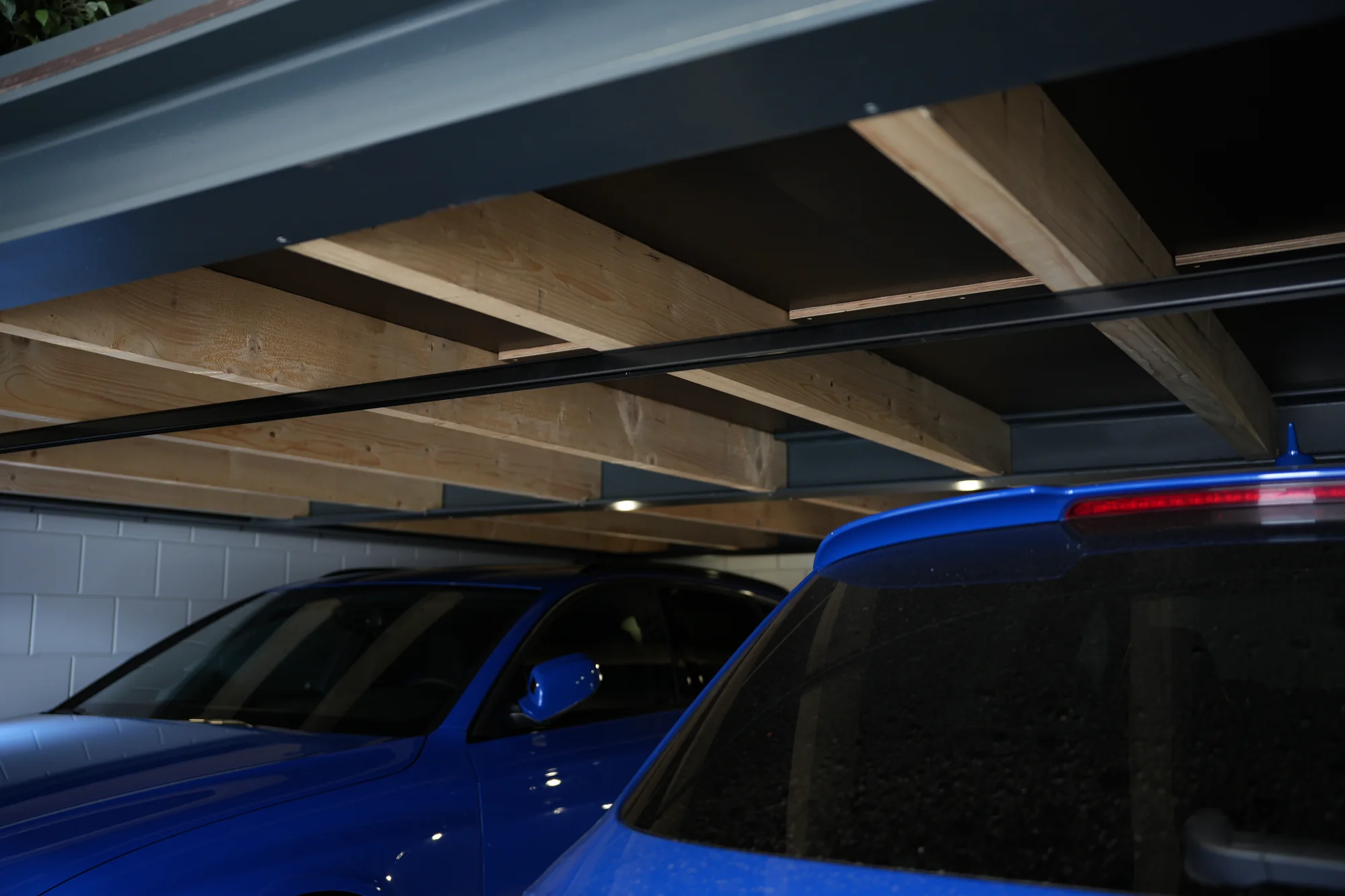 Stalen draagconstructie met houten balklaag boven een auto in een garage