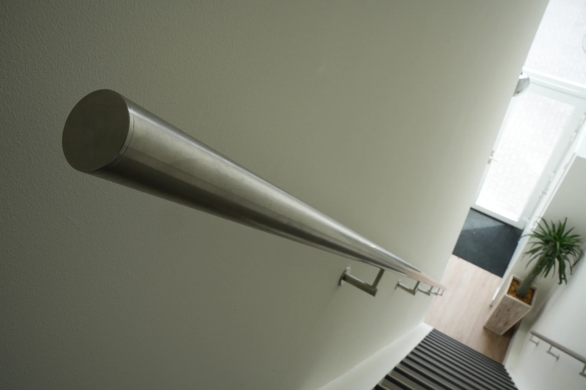 Minimalistische roestvaststalen trapleuning langs een witte wand